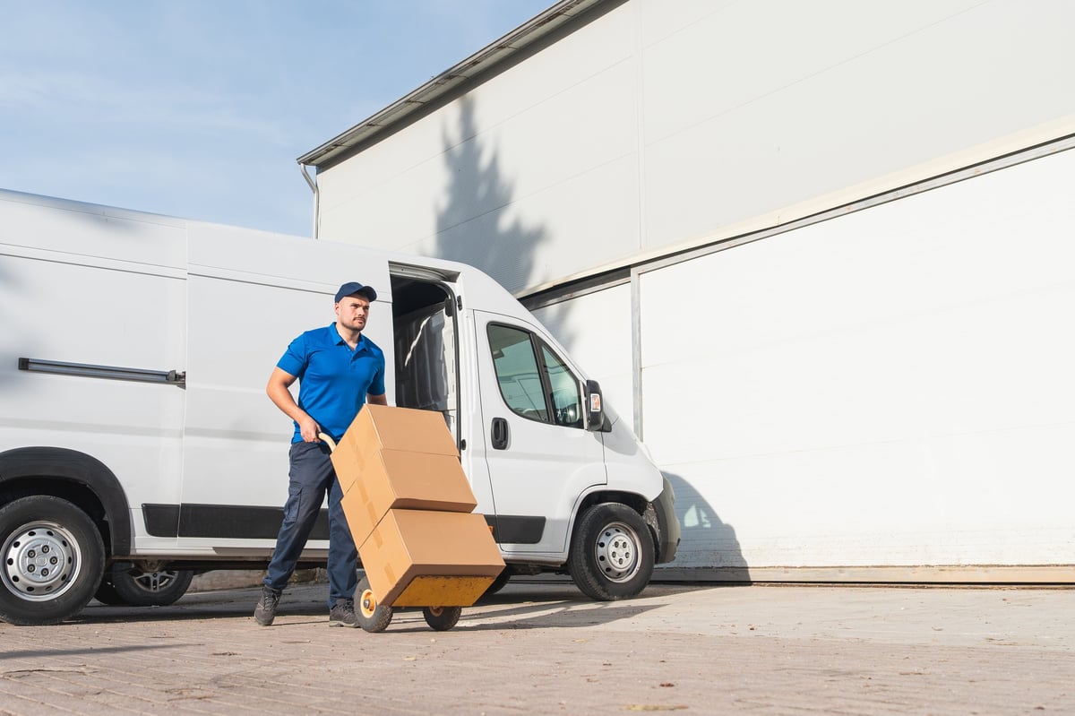 Delivery man transporting boxes outside a warehouse with a white van